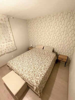 Ein Schlafzimmer mit einem bettenbezug mit Muster, einer Sitzbank am Fußende des Bettes, einem Nachttisch mit Lampe und einer Wand mit einem einzigartigen geometrischen Muster.