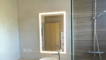 Une salle de bain moderne avec un lavabo blanc, un miroir avec éclairage intégré et une douche.