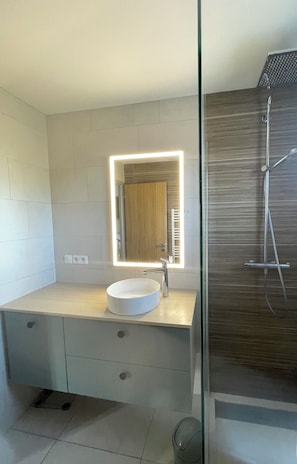 Une salle de bain moderne avec un lavabo blanc, un miroir avec éclairage intégré et une douche.
