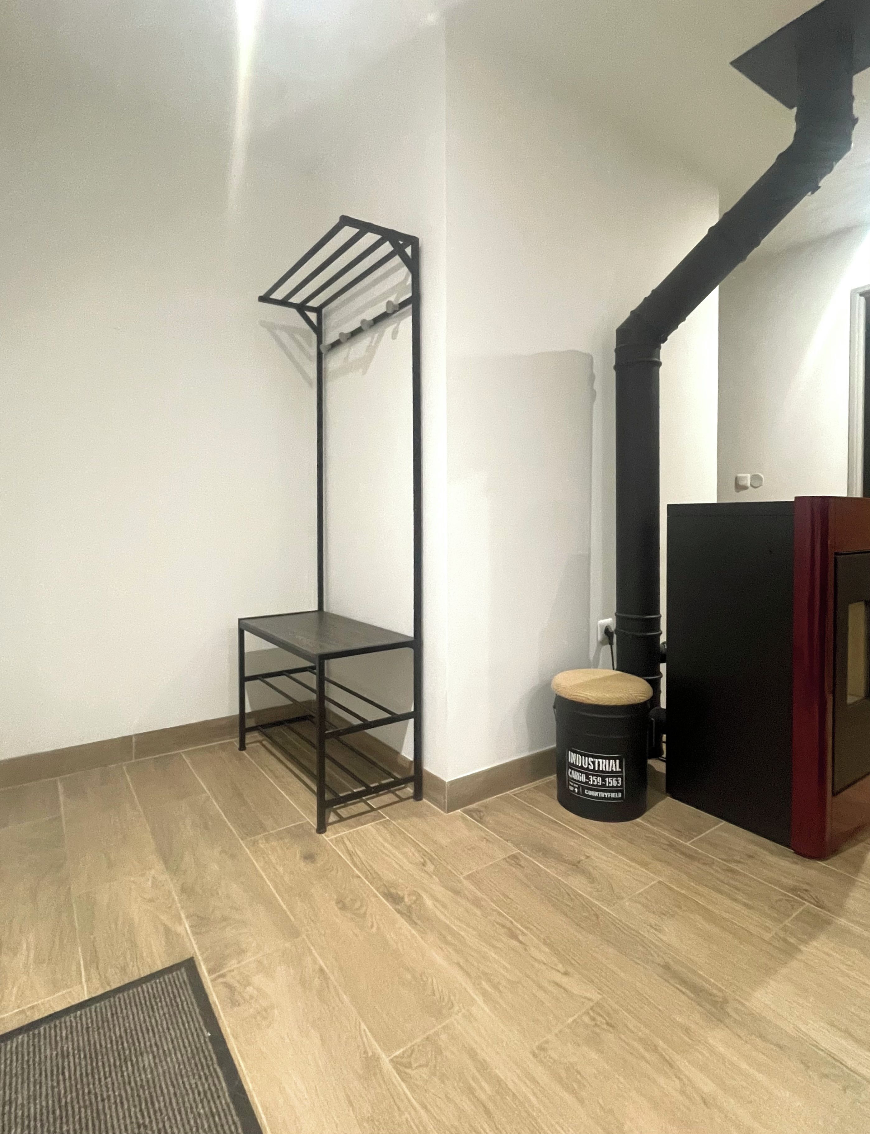 Une pièce avec une étagère en métal noir, une poubelle noire et un plancher en bois.