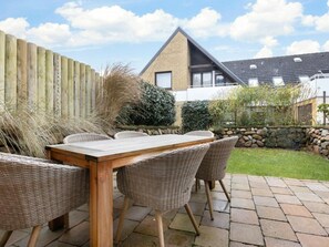 An outdoor patio with a wooden table and wicker chairs, a stone wall, and a wooden fence. - Holiday Home Watt'n Gluck - New! (Sylt)