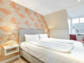 A bedroom with a bed, a nightstand, a lamp, and a window with a view of buildings. - Holiday Home Watt'n Gluck - New! (Sylt)
