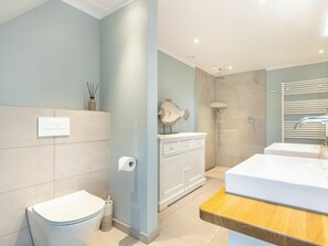 A bathroom with a toilet, a sink, a mirror, and a shower area. - Holiday Home Watt'n Gluck - New! (Sylt)