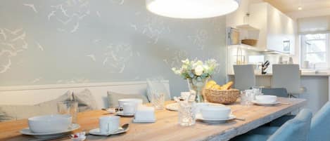 A dining area with a wooden table set for two, a vase with flowers, and a hanging light fixture.