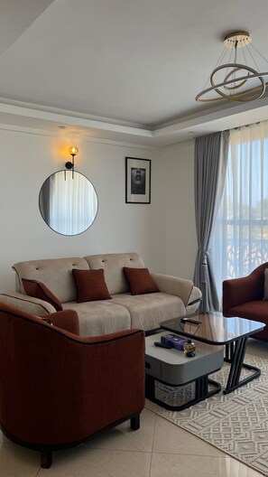 Uma sala de estar moderna com sofá, poltrona e mesa de centro. Há um quadro na parede e um lustre.