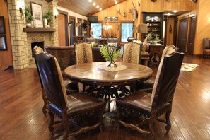 A dining area with a round table surrounded by leather chairs, a stone fireplace, and a wooden ceiling.