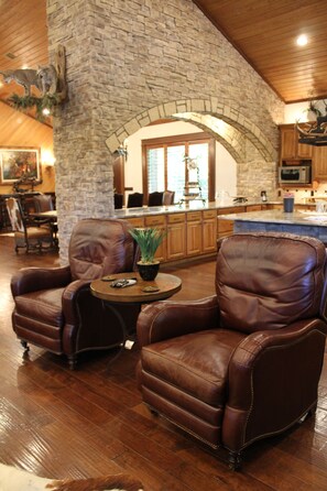 A spacious living area with leather armchairs, a stone wall, and a kitchen in the background.