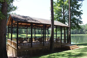 A covered outdoor seating area with tables and chairs, overlooking a lake and a golf course. - Private East Texas Ranch Retreat with 7 Cabins, Trophy Fishing & More (San Augustine)
