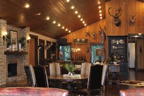 A dining area with a wooden ceiling, stone fireplace, and a wall adorned with mounted animal heads. - Private East Texas Ranch Retreat with 7 Cabins, Trophy Fishing & More (San Augustine)