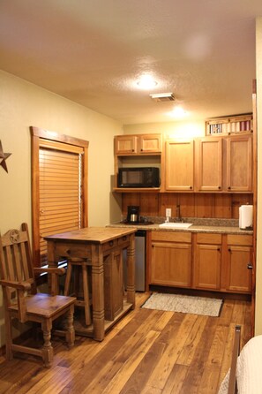 A compact kitchen with wooden cabinets, a microwave, a sink, and a dining area with a chair and table.
