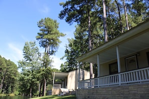A house with a porch, stone foundation, and a view of tall pine trees. - Private East Texas Ranch Retreat with 7 Cabins, Trophy Fishing & More (San Augustine)