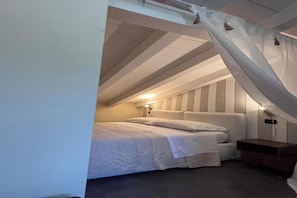 Ein kleiner, gemütlicher Raum mit schrägem Dach, einem Bett mit weißer Bettwäsche und einem Nachttisch.