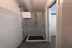 Ein Duschbereich mit Glaswänden und ein weißes Handtuch, das an der Tür hängt.