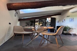 Ein Essbereich mit Tisch und Stühlen, einem Holzbalken an der Decke und Blick in einen anderen Raum.