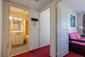A hotel room with a bathroom, a bed with a red and black bedspread, and a painting on the wall. - Apartment with balcony and swimming pool (Grasse)