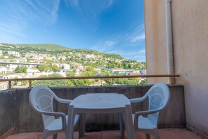 A balcony with a table and two chairs, overlooking a hillside town. - Apartment with balcony and swimming pool (Grasse)