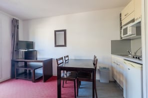 A compact room with a dining table, chairs, a television, a small kitchen area with a sink and microwave, and a trash bin. - Apartment with balcony and swimming pool (Grasse)