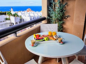 A balcony with a table set for breakfast, overlooking a coastal view with white buildings and a clear sky. - Vrbo Property (Adeje)