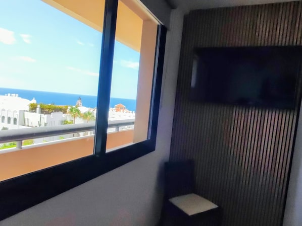 A room with a large window, a small table, and a wall-mounted TV. - Vrbo Property (Adeje)
