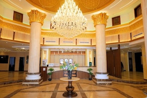 Un vaste hall d’entrée agrémenté d’un grand lustre, de colonnes en marbre et d’un comptoir d’accueil.