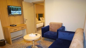 Et hotelværelse med fjernsyn, et skrivebord, et rundt bord og en blå sofa.