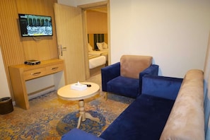 Une chambre d’hôtel équipée d’une télévision, d’un bureau, d’une table ronde et d’un canapé bleu.