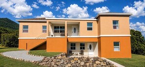 A two-story building with a flat roof, a covered front porch, and a stone pathway leading to the entrance. - Cozy 2-bedroom apartment in beautifuln Nevis (Charlestown)