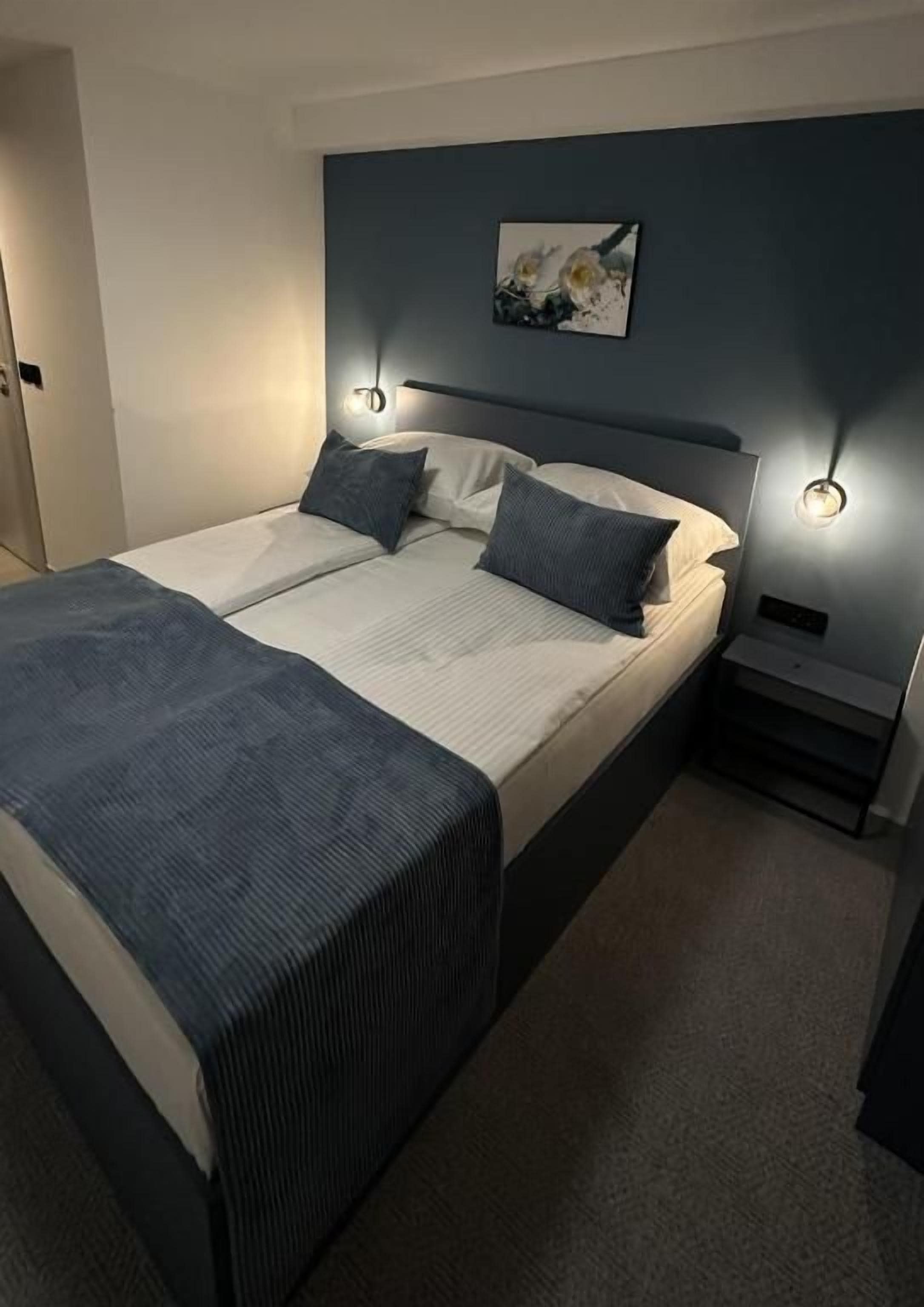 A double bed with a headboard, two bedside lamps, a wall-mounted artwork, and a bedside table.