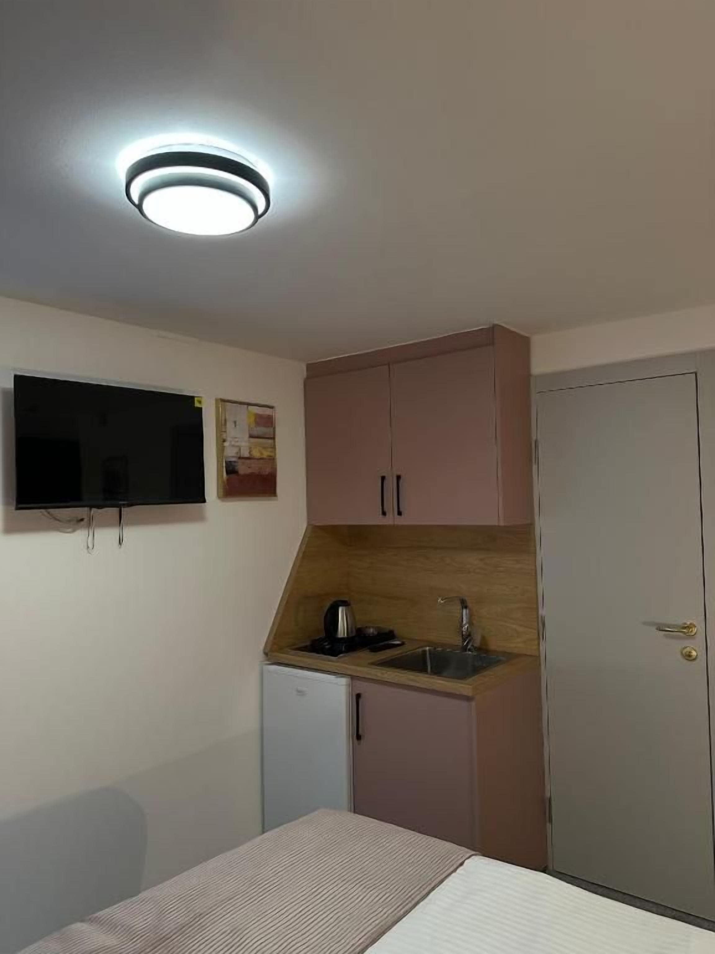 Une pièce de taille modeste comprenant un lit, une petite kitchenette avec un évier, un téléviseur et une porte.