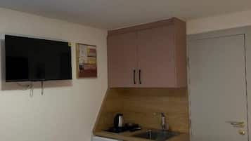Une pièce de taille modeste comprenant un lit, une petite kitchenette avec un évier, un téléviseur et une porte.