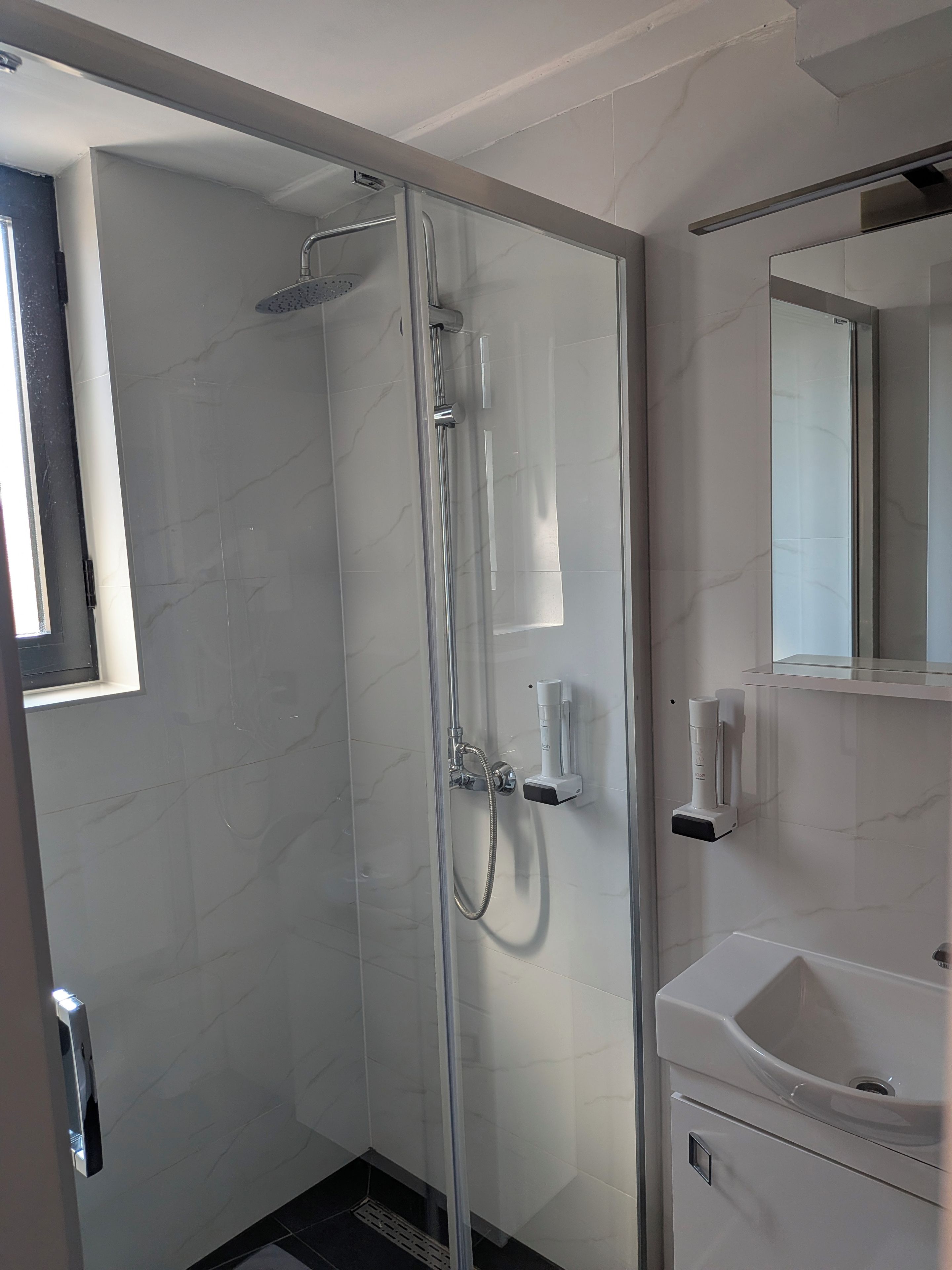 Une salle de bain moderne avec une douche à parois de verre, un lavabo blanc et un miroir au-dessus.