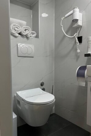 A bathroom with a toilet, towel rack, hairdryer, and a hand dryer. - Alinar Oasis Budget Hotel (Sarajevo)