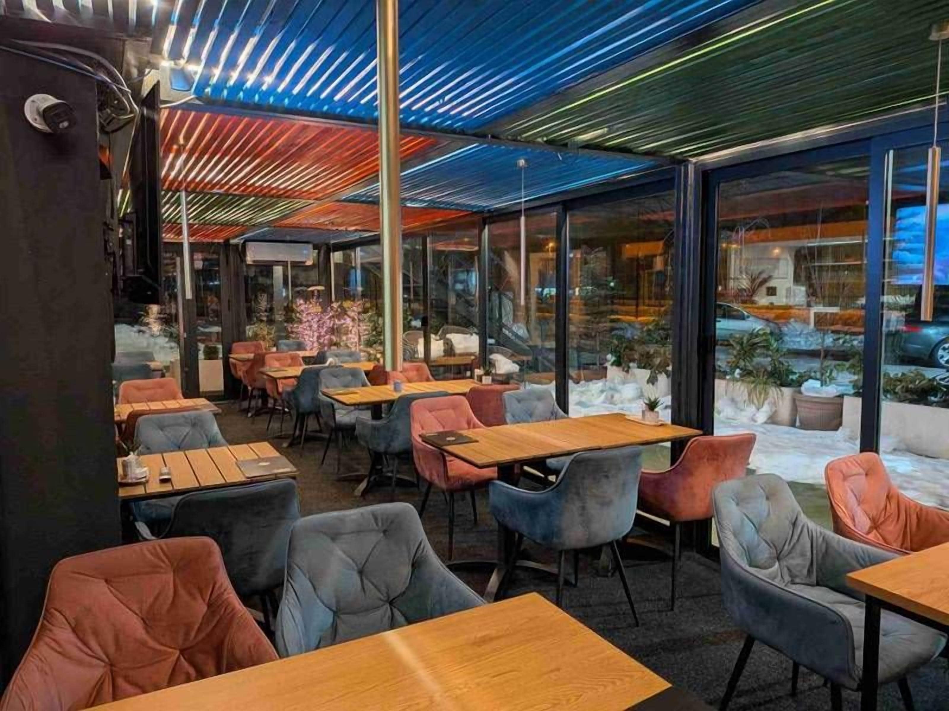 Un espace de détente intérieur avec des tables et des chaises, de grandes fenêtres et un plafond orné de motifs.