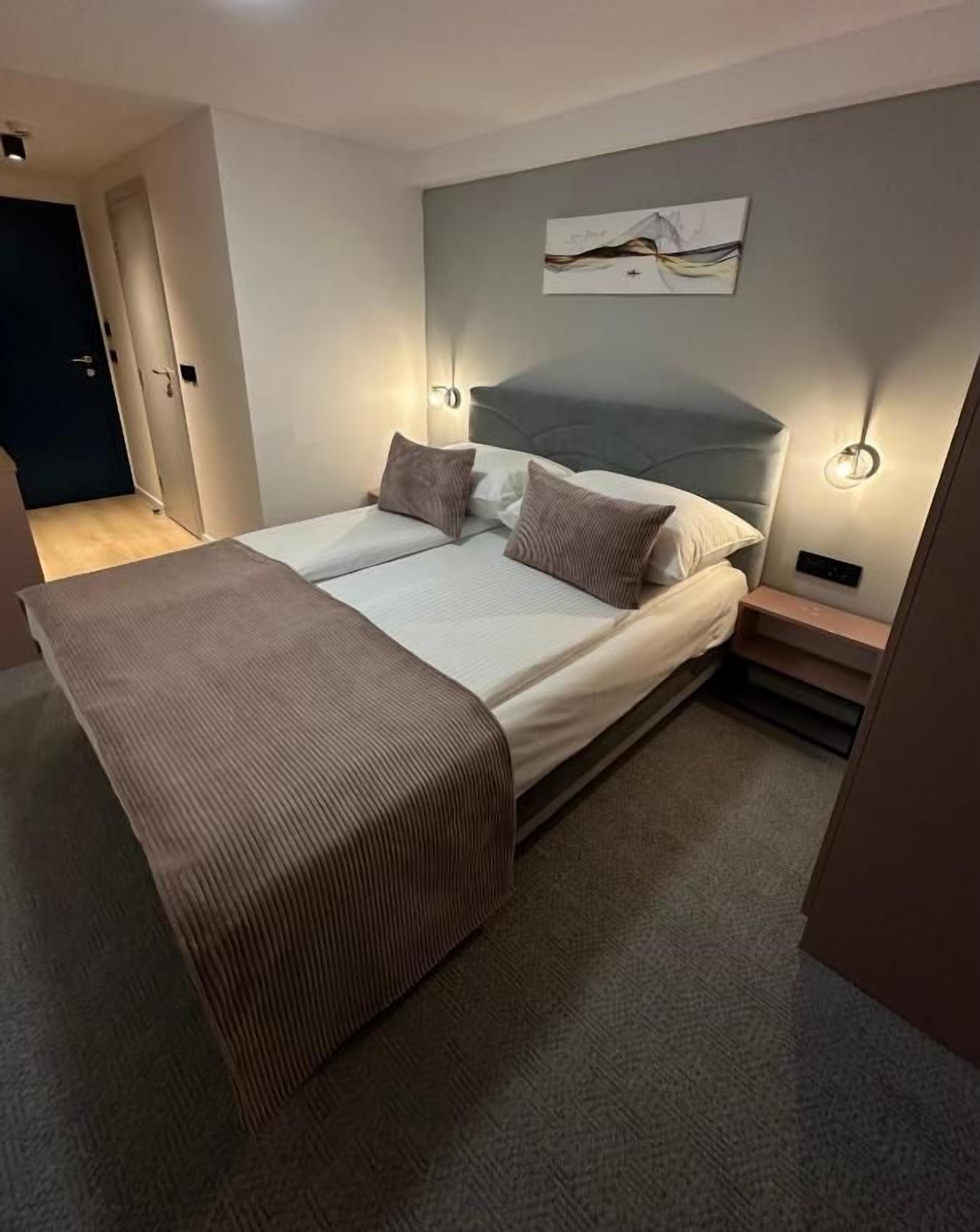 Un lit double avec une tête de lit, des tables de chevet et un luminaire fixé au mur.