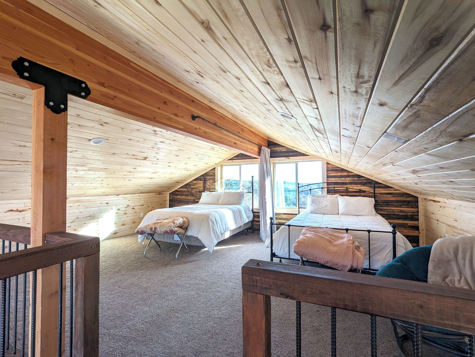 A cozy attic bedroom with two beds, a wooden ceiling, and a view of the outdoors.
