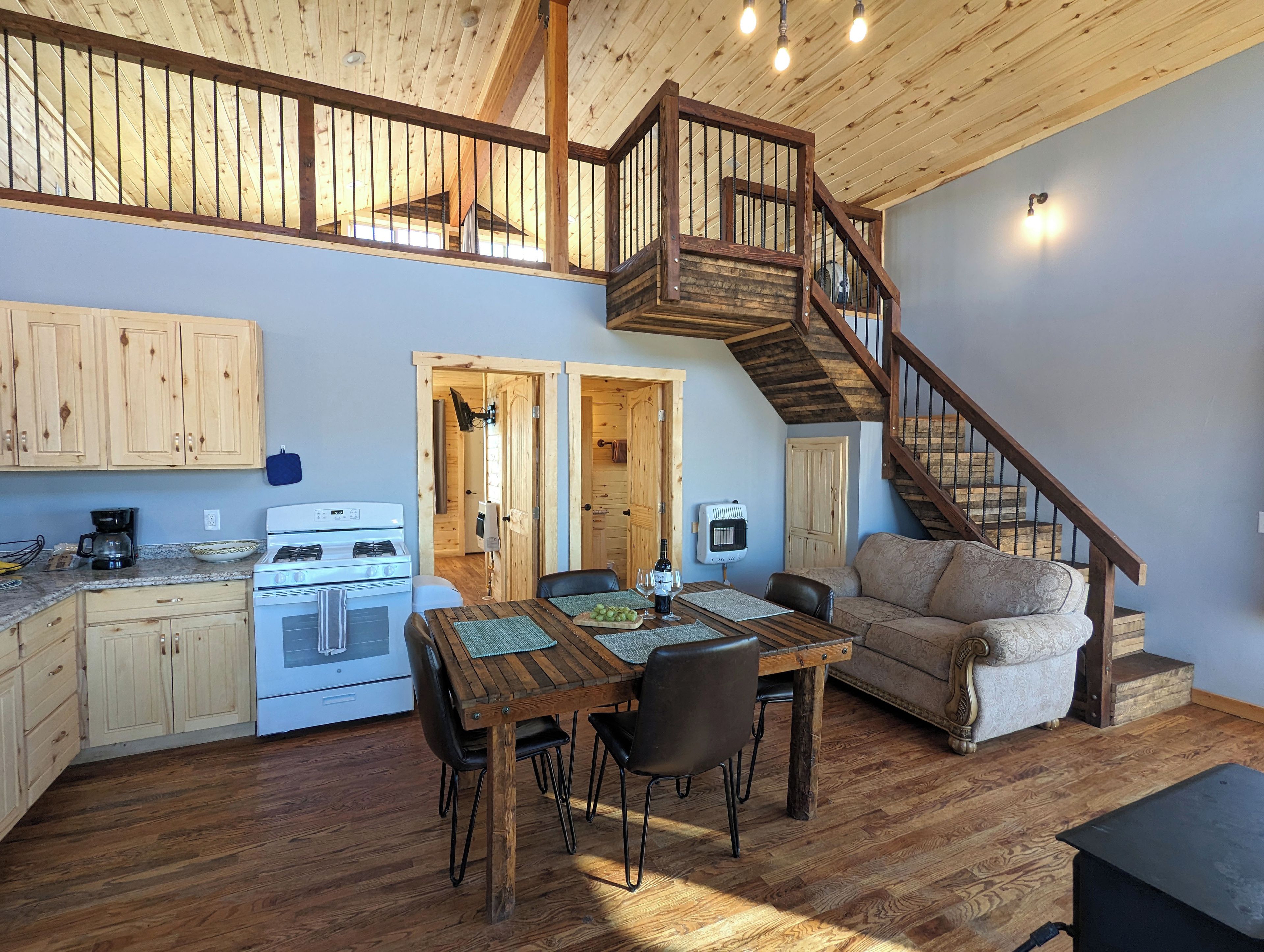 Une cuisine spacieuse avec des meubles de rangement en bois, une table à manger avec des chaises, un four encastré et un escalier en bois menant à l’étage supérieur.