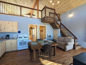 Une cuisine spacieuse avec des meubles de rangement en bois, une table à manger avec des chaises, un four encastré et un escalier en bois menant à l’étage supérieur.