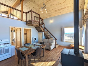 Cucina spaziosa con piano cottura, tavolo da pranzo e sedie. Una scala conduce a un piano superiore con un balcone.