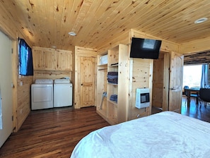 A wooden cabin interior with a bed, a washing machine, a TV, and a dining area. - Remote 2 bedrooms cabin (La Sal)