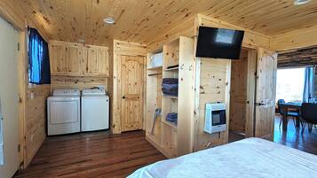 Un interior de madera con una cama, lavadora, televisor y zona de comedor.