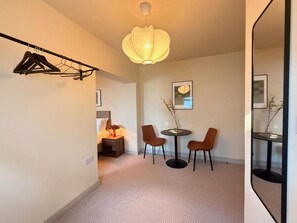 A hotel room with a bed, a bedside table, a mirror, a hanging clothes rack, and a pendant light.