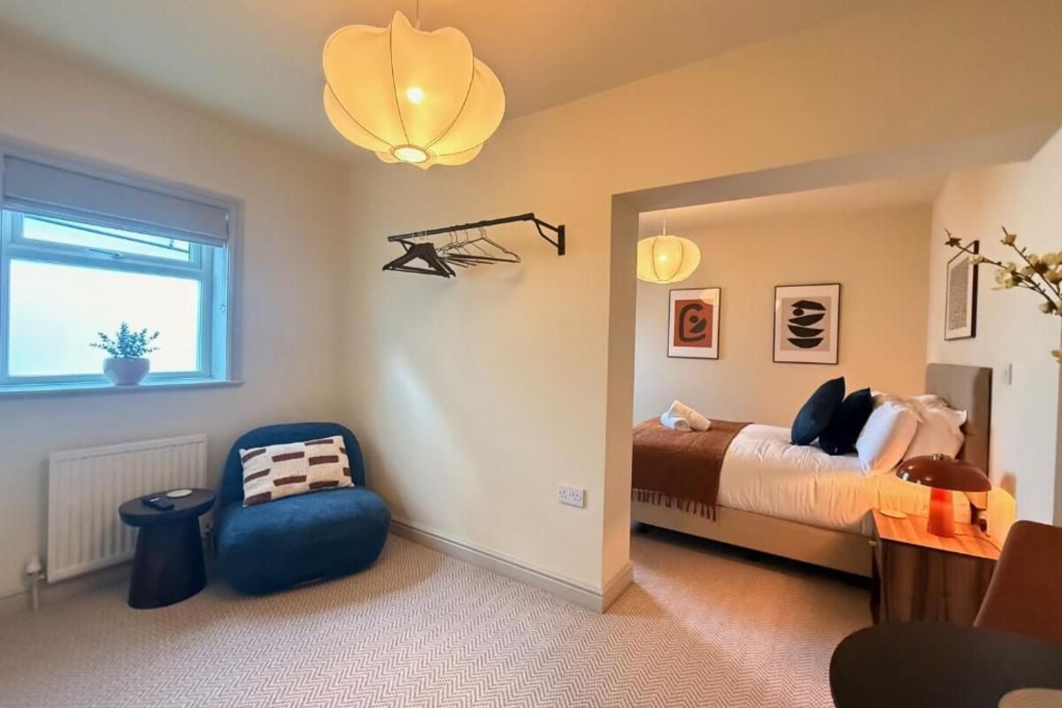 A modern bedroom with a bed, a blue armchair, a small table, and a hanging light fixture.