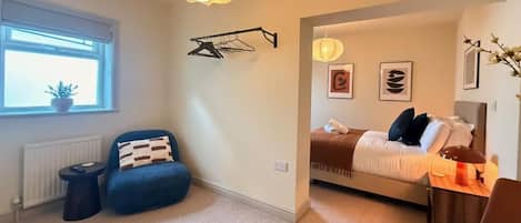 Un dormitorio moderno con cama, un sillón azul, una mesita y una lámpara colgante.