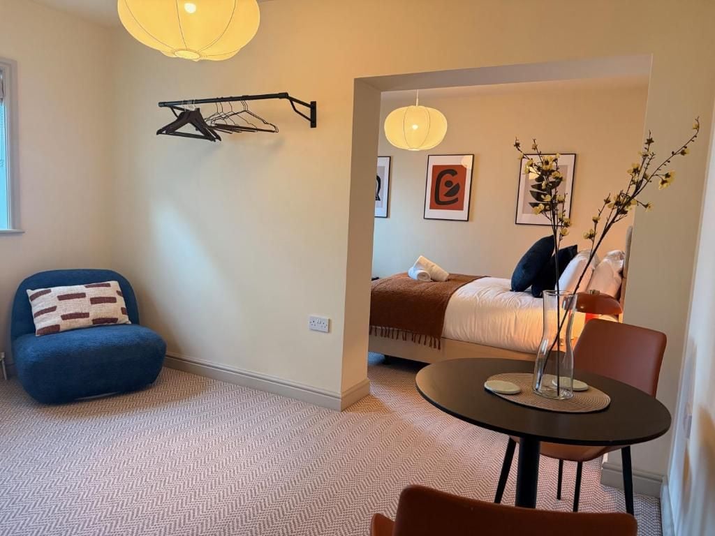Un dormitorio moderno con cama, una silla, una mesa y una lámpara colgante.