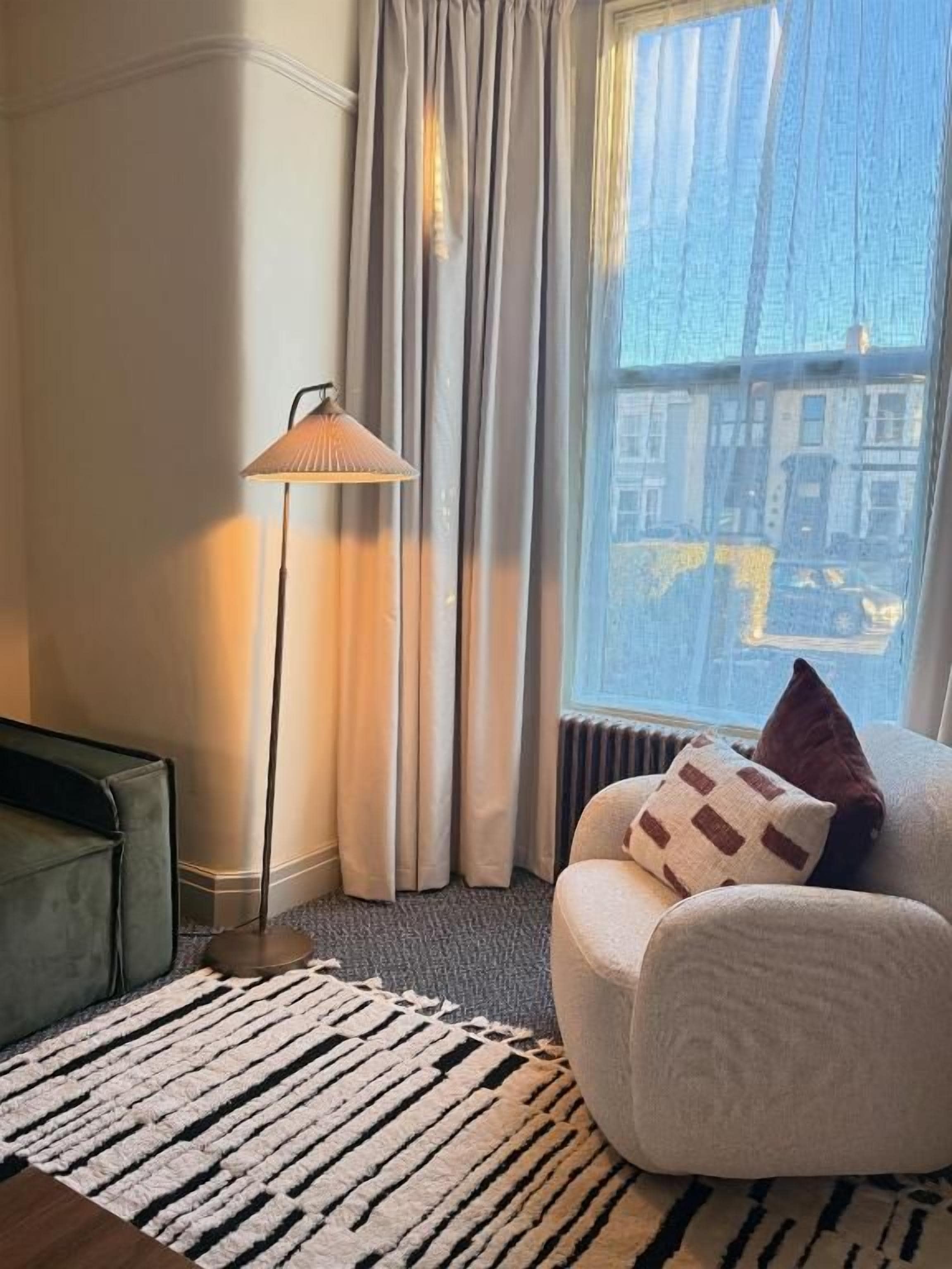 A room with a sofa, a floor lamp, a patterned rug, and a view through a window.