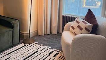 A room with a sofa, a floor lamp, a patterned rug, and a view through a window.