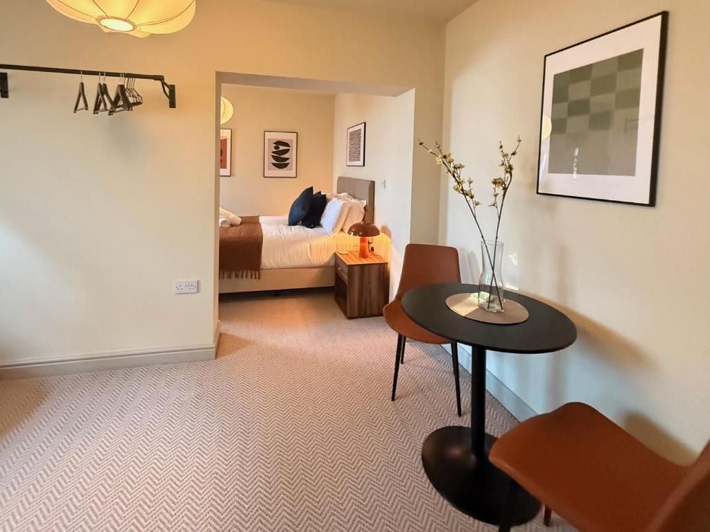 Ein Hotelzimmer mit einem Bett, einem Schreibtisch und einem Stuhl. Ein Fenster bietet einen Ausblick, es gibt eine Lampe und eine Vase mit Ästen.