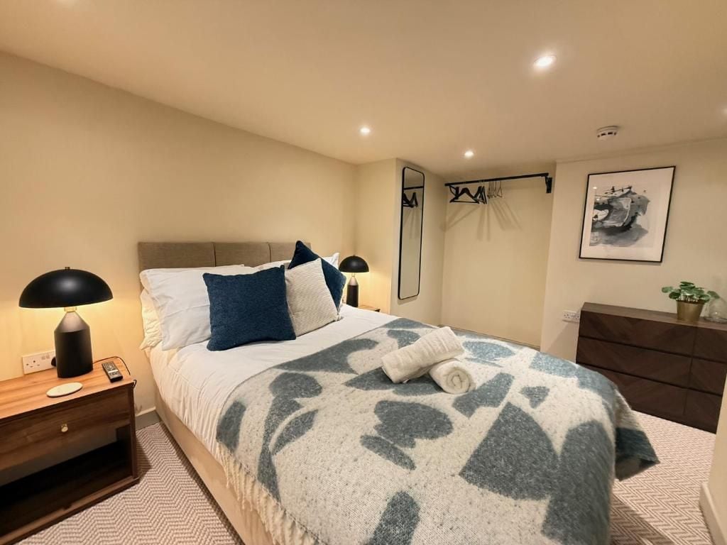 A hotel room with a bed, bedside table, lamp, mirror, dresser, and a framed picture on the wall.