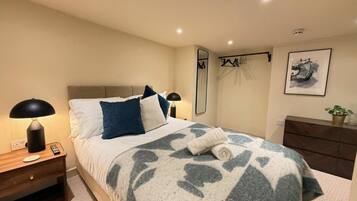 A hotel room with a bed, bedside table, lamp, mirror, dresser, and a framed picture on the wall.