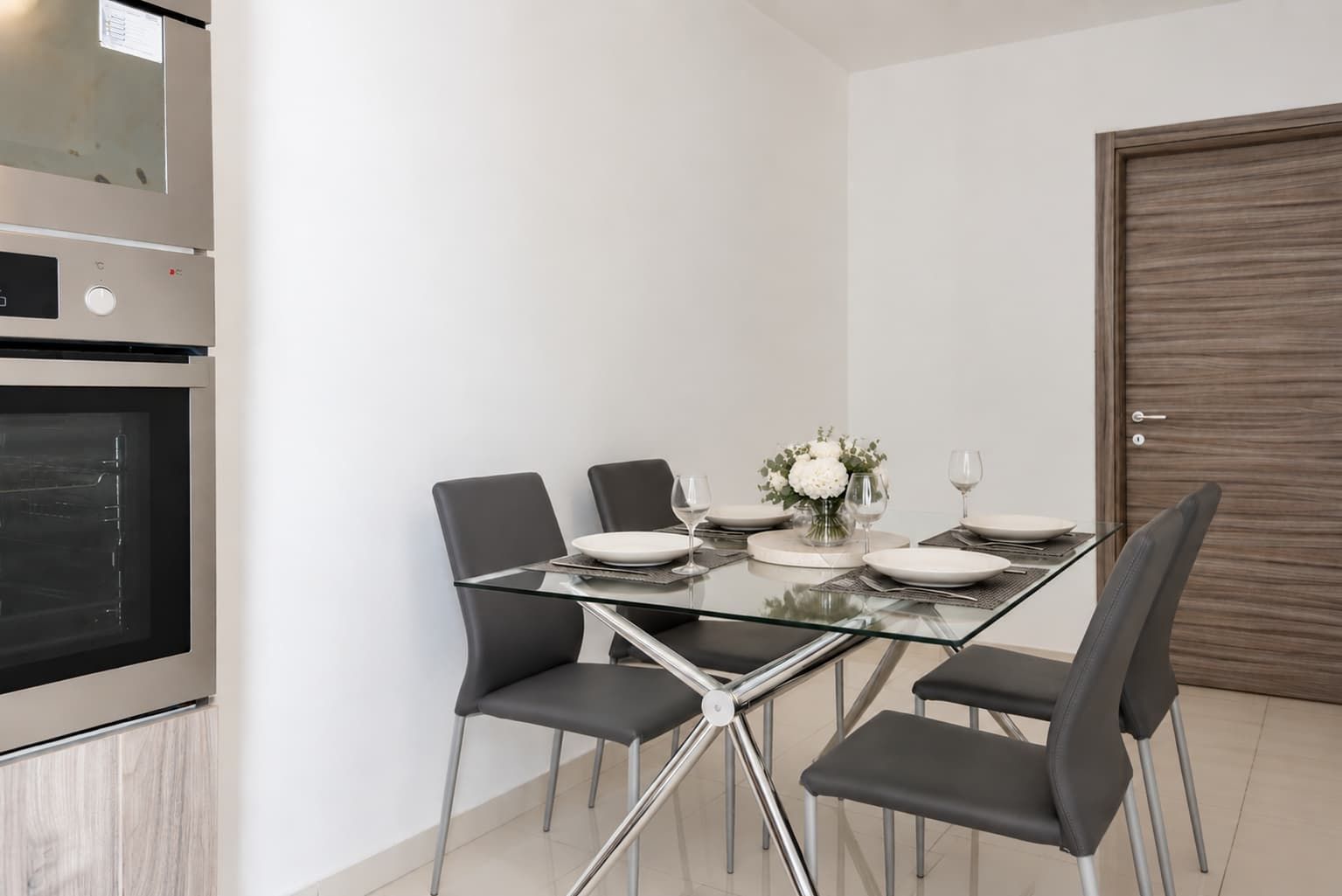 A modern dining area with a glass table, six chairs, and a wooden door.